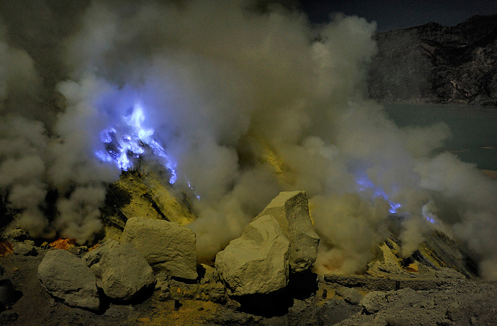 Кислотные вулканические газы выделяются из отверстий среди желтых кусков серы и горящей жидкой серы на Кава Иджен.