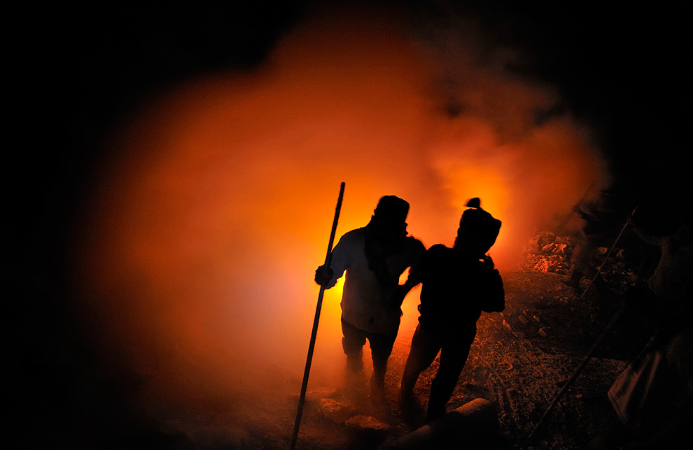 Шахтеры отдыхают возле огня, держа длинные ломы. Они используют их для добычи серы в кратере.